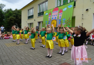 Taras przedszkolny, a na nim scenografia przedstawiająca zamek. Dzieci tańczą z rękoma uniesionymi w górę.
